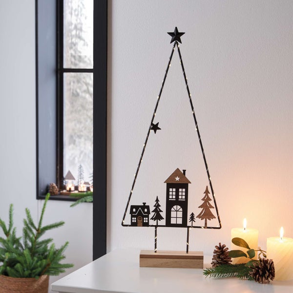 Dekorativer Weihnachtsbaum aus Metall mit Beleuchtung auf einem Tisch, umgeben von Kerzen und Tannenzapfen.