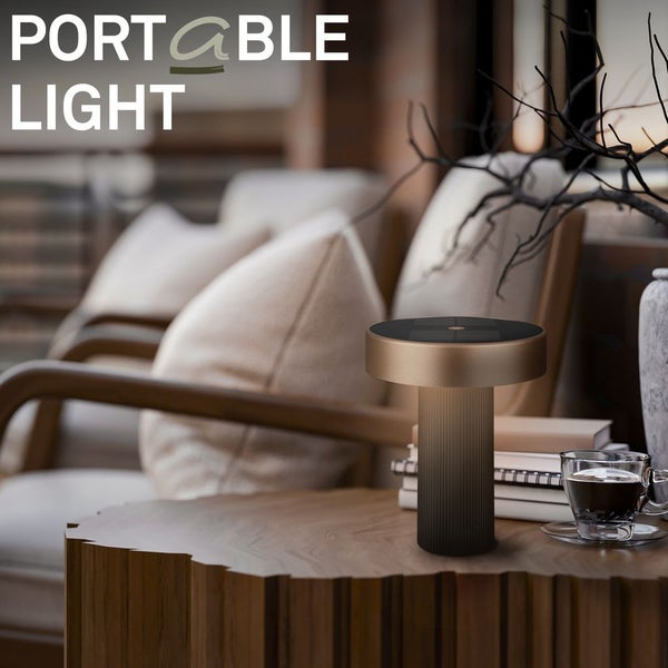 Tragbare kabellose Tischleuchte mit Metalloberfläche auf einem hölzernen Beistelltisch in einem gemütlichen Wohnbereich.