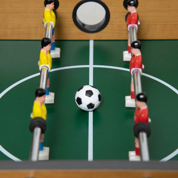 Tischfußballspiel mit grünem Spielfeld, Fußball und Spielerfiguren an Metallstangen.