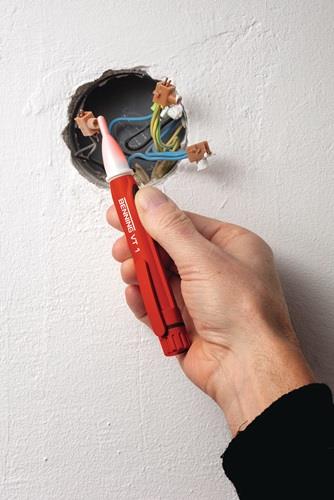 Hand prüft mit Spannungsprüfer die Stromzufuhr an einer Wand