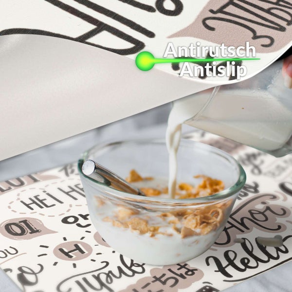 Platzset mit Antirutsch-Funktion und verschiedenen internationalen Grußworten, abgebildet mit einer Schüssel Müsli und Milch.