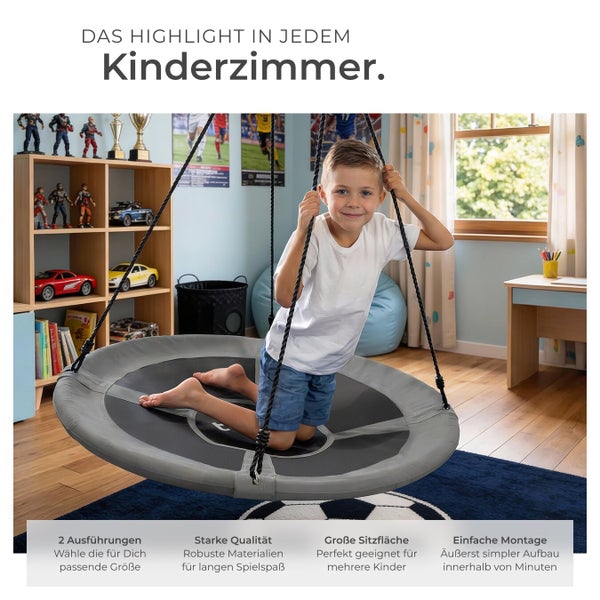 Kind kniet auf einer runden Nestschaukel in einem hellen Kinderzimmer mit Holzregal und Spielzeug