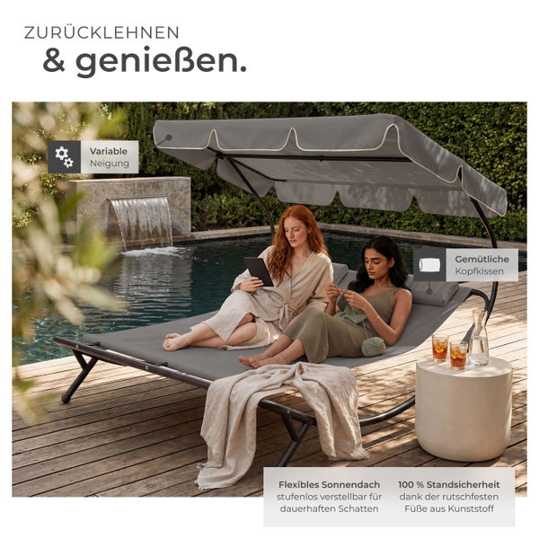 Graue Doppelsonnenliege mit verstellbarem Sonnendach und Kopfkissen auf einer Holzterrasse am Pool. Zwei Frauen entspannen auf der Liege.