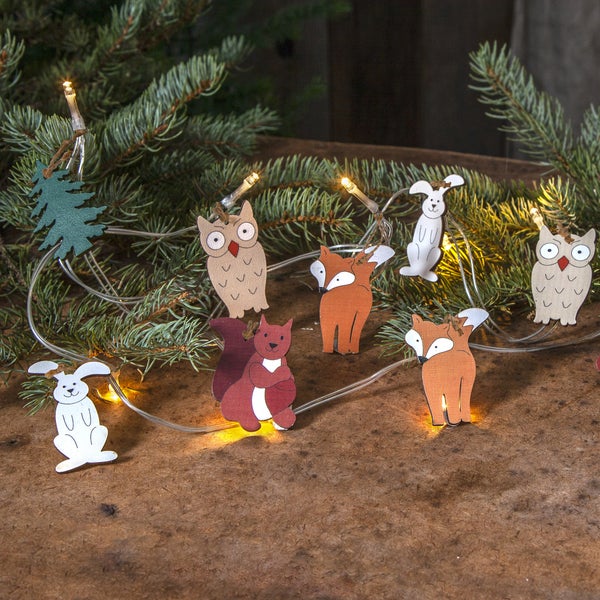 Dekorative Holzanhänger mit Tiermotiven und Lichterkette vor Tannenzweigen