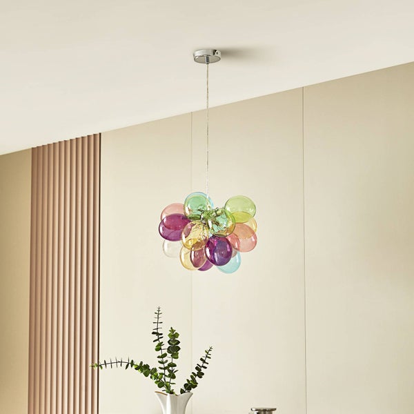 Moderne Pendelleuchte mit bunten Glaskugeln in einem hellen Raum mit vertikalen Wandlamellen und einer Pflanze.