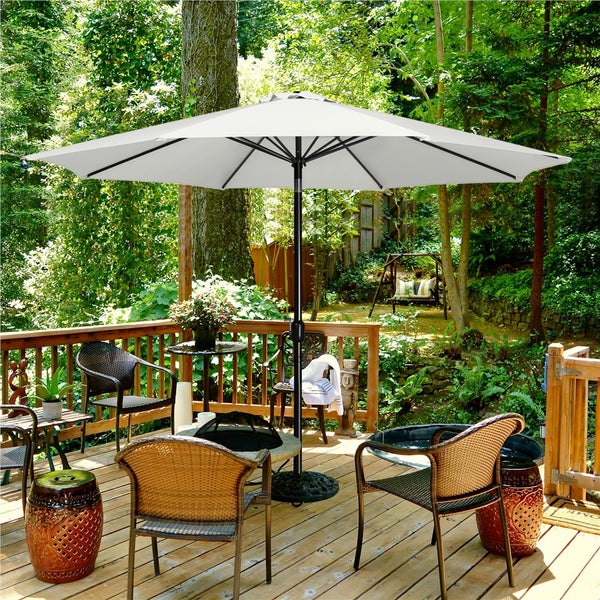 Szene mit weißem Sonnenschirm, Gartenmöbeln und üppigem Grün auf einer Holzterrasse.