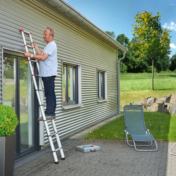 Mann auf einer Mehrzweckleiter vor einem Haus bei der Arbeit