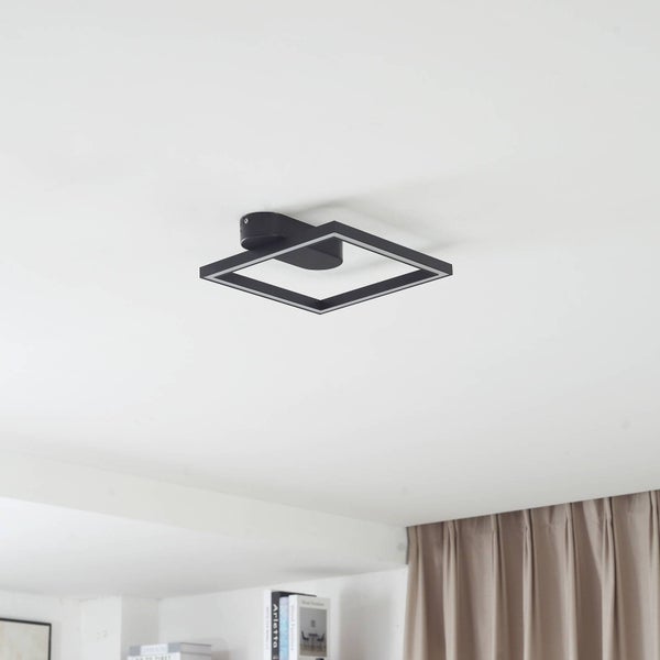 Moderne quadratische LED-Deckenleuchte in Schwarz an einer weißen Decke in einem hellen Raum mit Vorhang und Bücherregal.
