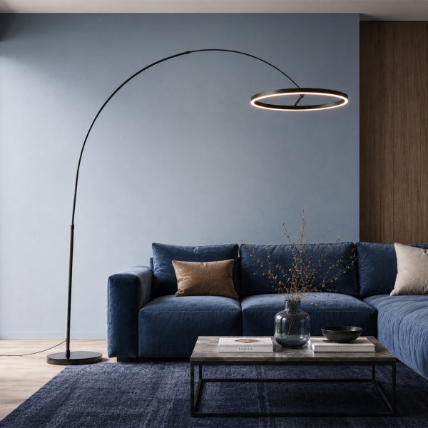 Moderne Bogenlampe mit ringförmigem LED Leuchtkopf steht neben einem komfortablen Sofa in einem stilvoll eingerichteten Wohnbereich.
