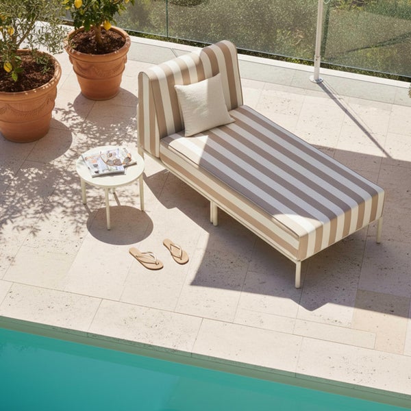 Gestreifte Gartenliege mit Polsterauflage auf einer hellen Terrasse am Pool, kleiner Beistelltisch und Pflanzen im Hintergrund.