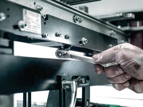 Hand hält einen Ratschenschlüssel an einer Maschine