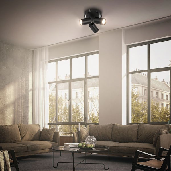 Dreiflammige Deckenleuchte in Schwarz in einem hellen, modern eingerichteten Wohnzimmer mit großen Fenstern und gemütlichen Sofas.