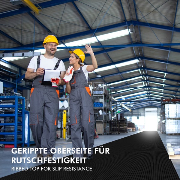 Arbeiter mit Sicherheitsausrüstung auf einer gerippten Gummimatte in einer Werkshalle