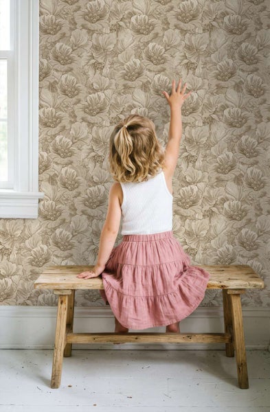 Kind sitzt auf einer rustikalen Holzbank vor einer Wand, die mit einer Vliestapete mit floralem Blumenmuster im klassischen Stil tapeziert ist.