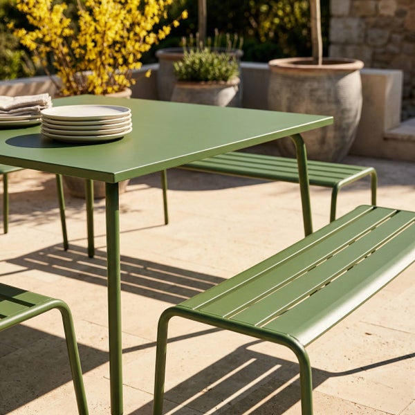 Moderner Gartentisch und Bänke aus grünem Metall auf einer hellen, organisierten Terrasse mit großen Pflanzgefäßen.