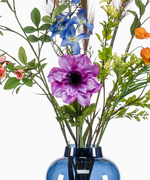 Künstlicher Blumenstrauß mit rosa Rosen, blauen Blüten und einer violetten Anemone in einer blauen Glasvase.