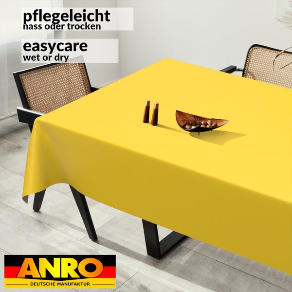 Abwischbare Tischdecke auf Esstisch in hellem Raum. Pflegeleicht nass oder trocken zu reinigen. Stühle mit Geflecht. ANRO Logo.