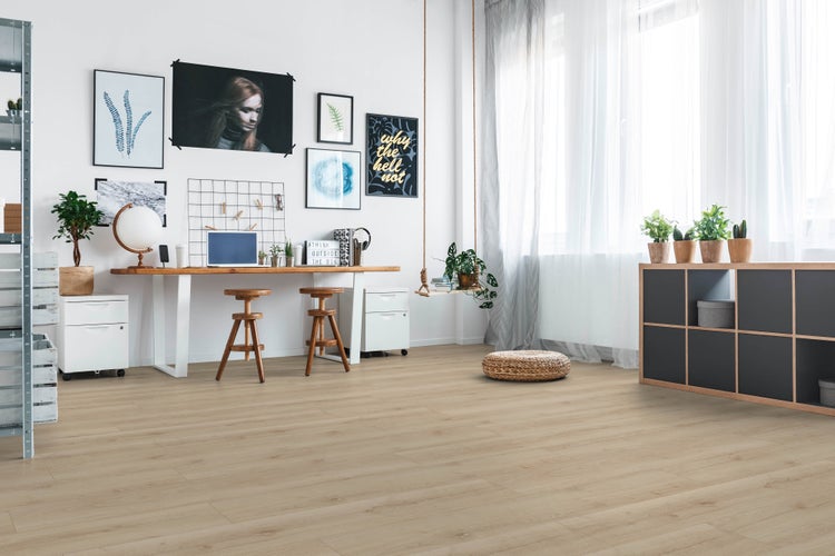 Ein moderner Wohn- und Arbeitsbereich mit hellem Holzoptik-Laminatboden, weißem Schreibtisch, Hockern, Regalen und hängender Zimmerpflanze.