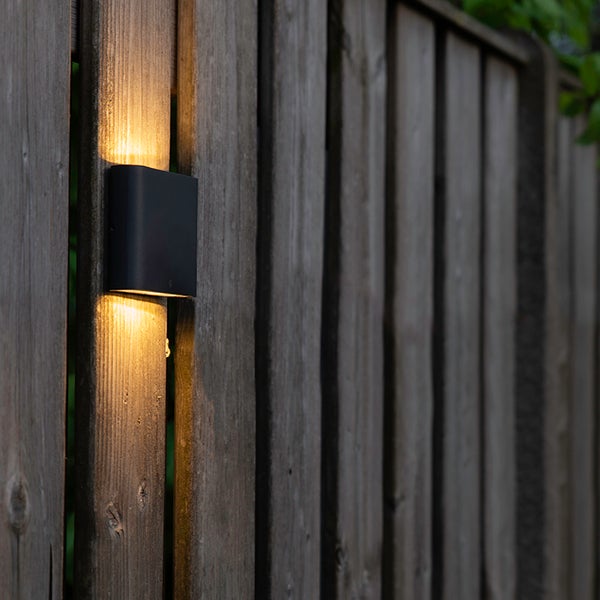 Außenwandleuchte an einem Holzzaun mit Lichtstrahl nach oben und unten.