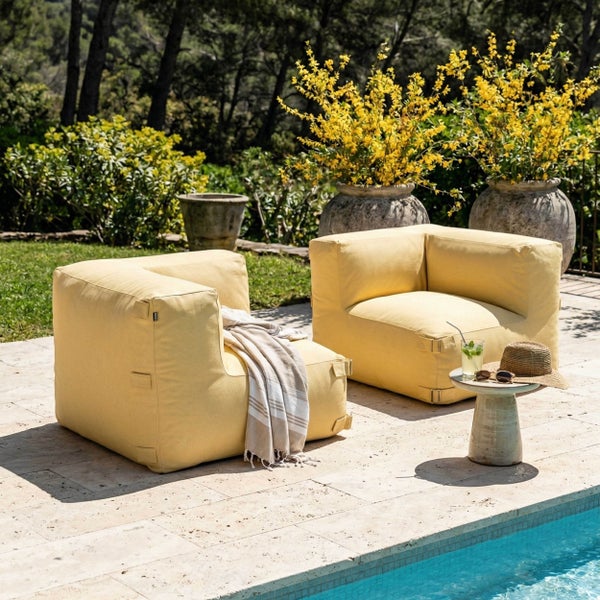 Zwei gelbe Outdoor-Sitzsäcke in Sesselform auf einer hellen Steinterrasse am Pool, helle Atmosphäre mit Pflanzen und einem Beistelltisch.