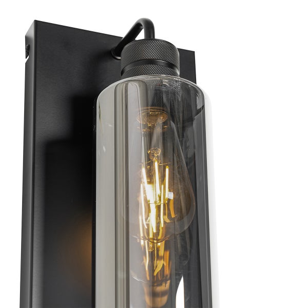 Wandleuchte mit schwarzer Metallhalterung, zylindrischem Glasschirm und dekorativem LED-Leuchtmittel.