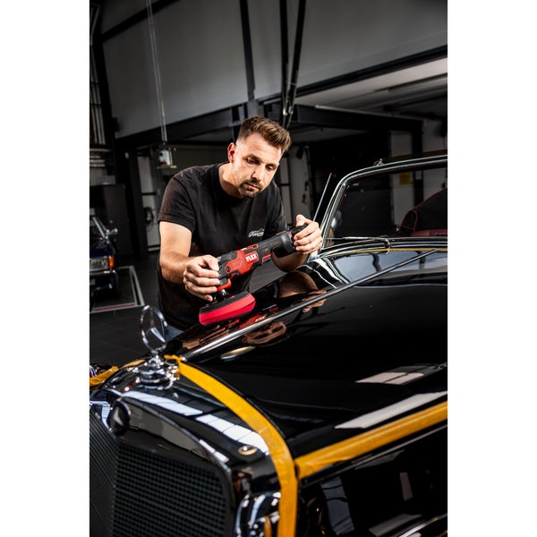 Ein Mann poliert die Motorhaube eines schwarzen Oldtimers mit einer Flex Poliermaschine in einer professionellen Werkstatt.
