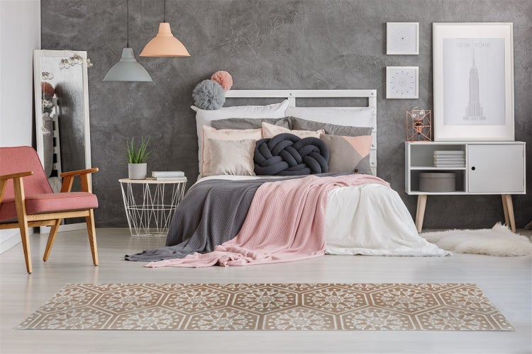 Modernes Schlafzimmer mit grauer Strukturwand, weißem Bett, rosa Sessel und einem Bodenläufer mit geometrischem Blumenmuster.