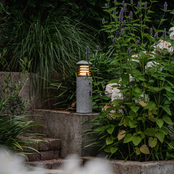Moderne Sockelleuchte in Steinoptik im Garten platziert, umgeben von Pflanzen und Blumen für eine stimmungsvolle Außenbeleuchtung.