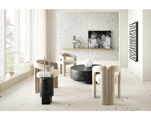Modernes, helles Wohnzimmer mit drei Polstersesseln, rundem Couchtisch und Wänden in Terrazzo-Optik.