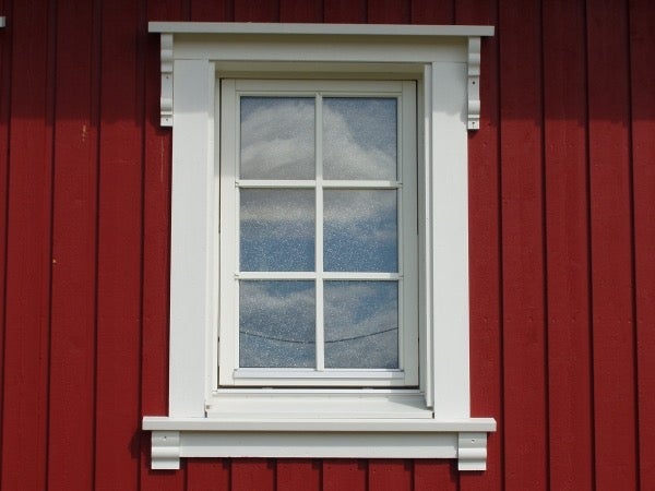Ein einzelnes Holzfenster mit Sprossen und verzierten Holzrahmen in einer senkrecht verschalten Fassade.