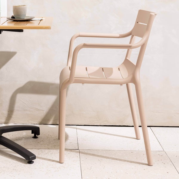 Moderner Gartenstuhl mit Armlehnen aus Kunststoff, Sitzfläche und Rückenlehne in Lattenoptik an einem Tisch.