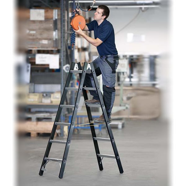 Eine Person steht auf einer Sprossenleiter in einem Lagerhaus und justiert eine Vorrichtung.