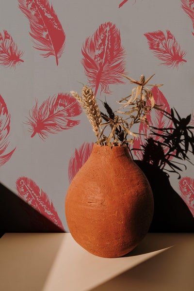 Eine runde Terrakotta Vase mit Trockenblumen steht vor einer Tapete mit Feder Muster.