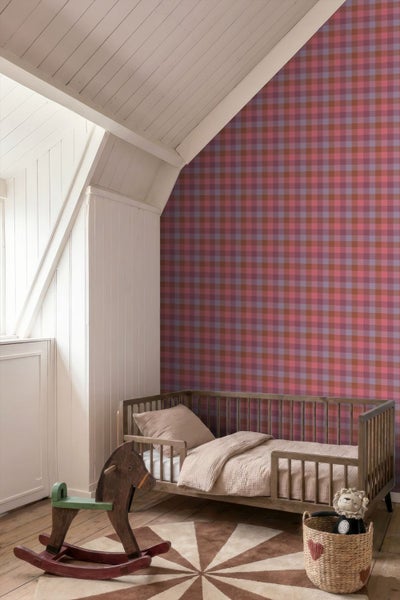 Kinderzimmer im Dachgeschoss mit karierter Tapete in Rot-, Rosa- und Brauntönen, Holz-Kinderbett, Schaukelpferd und gemustertem Teppich.