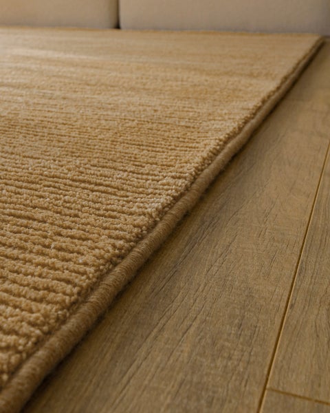 Beigefarbener Teppich mit Rippenstruktur auf Holzfußboden.