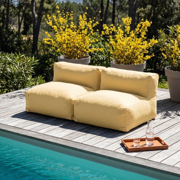 Gelbes Zweisitzer Outdoor Lounge Sofa aus Stoff auf einer Holzterrasse an einem Pool mit blühenden Pflanzen im Hintergrund