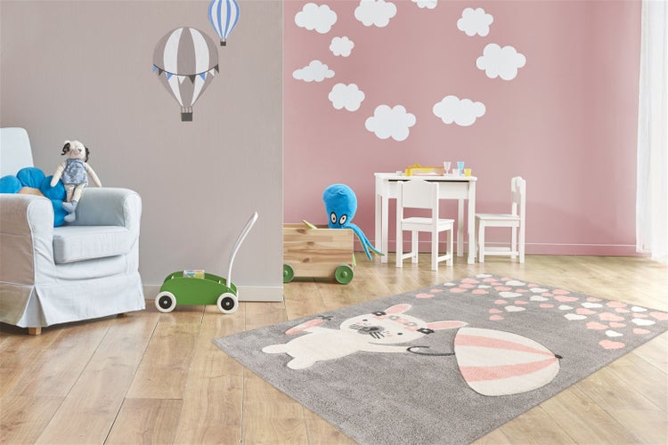 Ein Kinderteppich mit Hasenmotiv und Regenschirm in einem spielerisch gestalteten Kinderzimmer mit Möbeln und Spielzeug auf einem Holzboden.