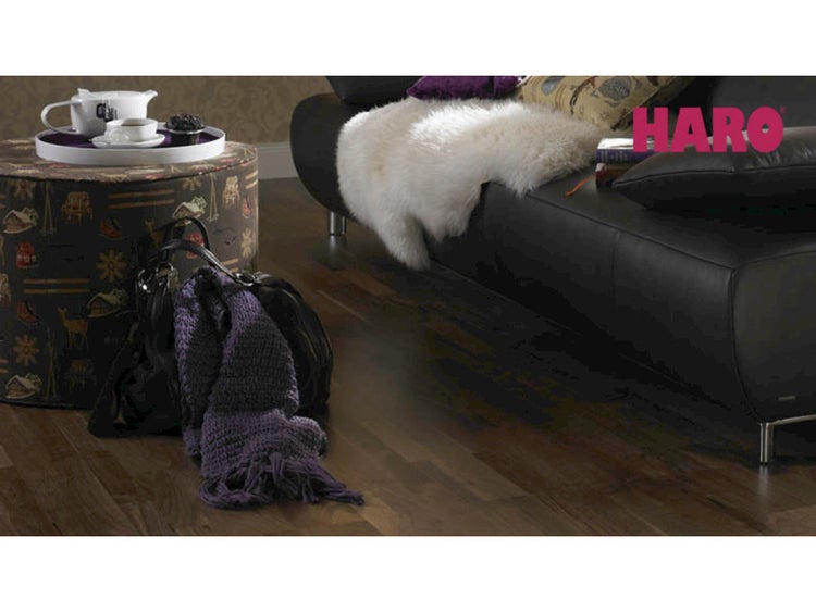 Dunkler Parkettboden von Haro in einem wohnlichen Zimmer mit Ledersofa, Schaffell und Teetablett. Haro Logo.