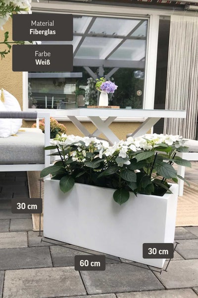 Weißer Fiberglas-Pflanzkasten mit weißen Blumen auf einer Terrasse. Maße: 60 Zentimeter Länge, 30 Zentimeter Höhe, 30 Zentimeter Breite.