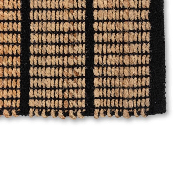 Detailansicht eines schwarz und beige gewebten Teppichs mit Streifenmuster und grober Struktur aus Naturfasern.