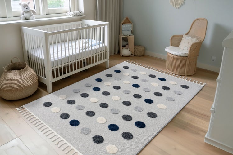 Ein Kinderzimmer mit einem rechteckigen Teppich mit Punktemuster, einem weißen Gitterbett, einem Rattan-Sessel und einem gewebten Aufbewahrungskorb.