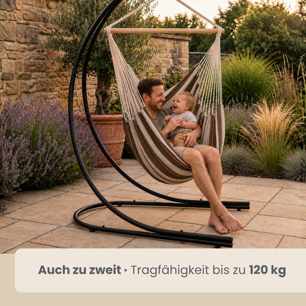 Vater und Kind sitzen gemeinsam in einer Hängematte mit Gestell auf einer Steinterrasse im Garten