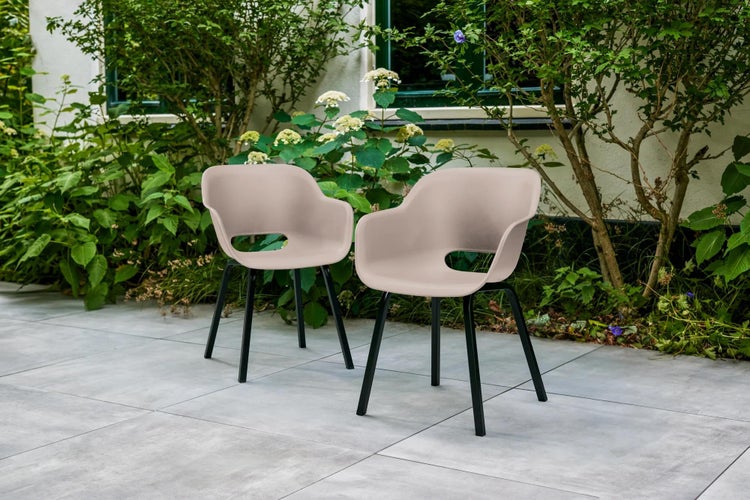 Zwei moderne Armlehnstühle mit beigefarbenen Sitzschalen und schwarzen Metallbeinen auf einer gefliesten Gartenterrasse.