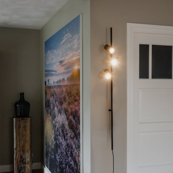 Schmale Wandleuchte mit drei Lichtquellen neben einem Gemälde im Flur