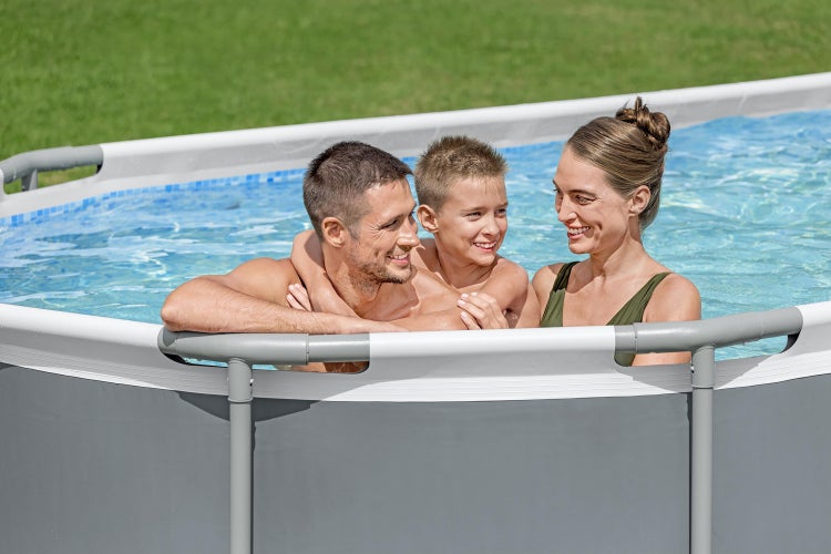 Eine Familie lächelt in einem Aufstellpool mit grauem Rahmen, weißem Rand und blauer Mosaik-Innenfolie im grünen Garten.