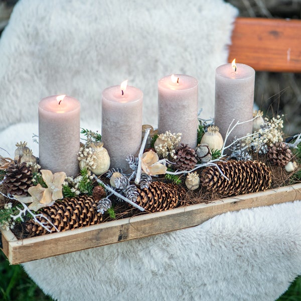 Adventskranz mit vier brennenden Kerzen, Tannenzapfen und Dekoration in einer Holzschale