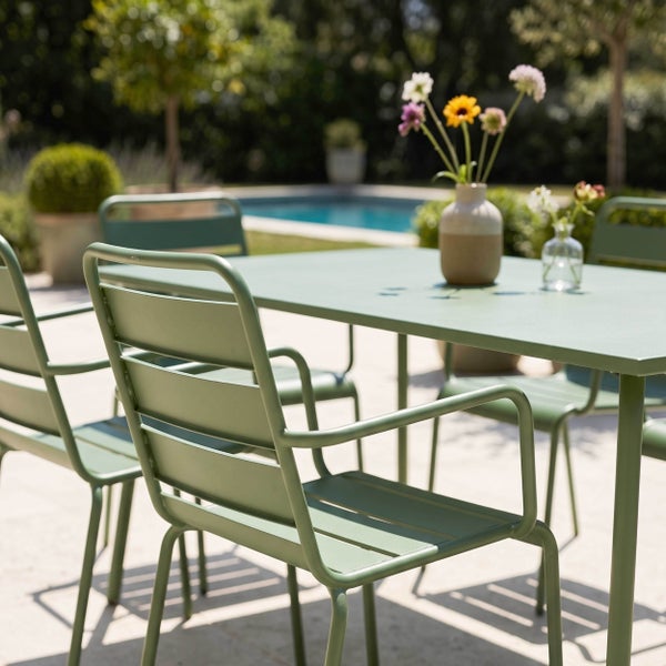 Moderne grüne Garten-Essgruppe aus Metall auf einer hellen, sonnigen Terrasse neben einem Pool.