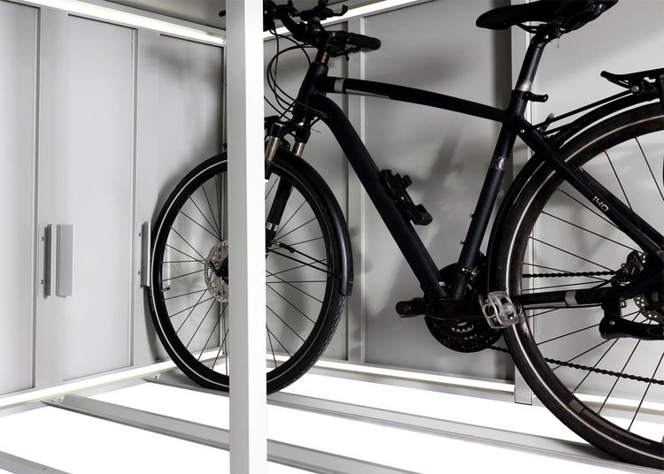 Fahrrad in einer Metall-Fahrradbox mit integrierten LED-Lichtleisten am Boden und an der Decke.