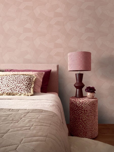 Helles Schlafzimmer mit geometrischer Tapete, Bett mit Kissen und Tischlampe auf einem gemusterten Hocker.