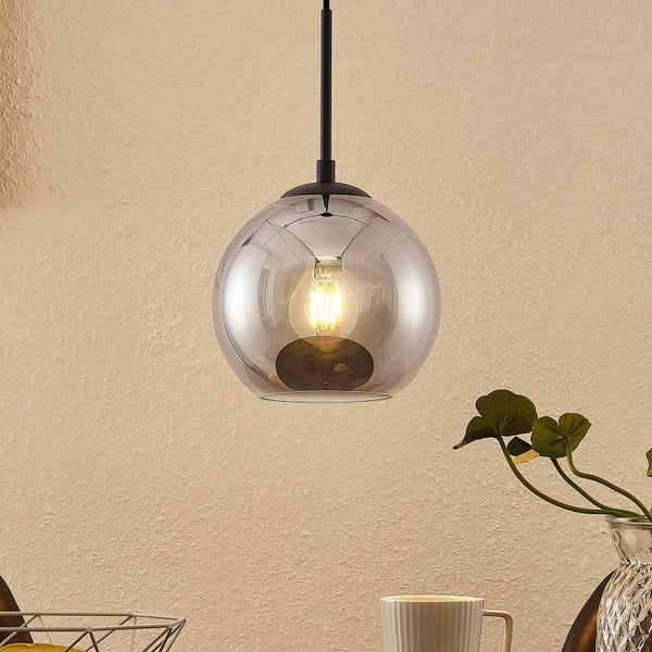 Kugelförmige Pendelleuchte aus Rauchglas mit sichtbarem Filament-Leuchtmittel und schwarzer Halterung vor einer hellen, strukturierten Wand.